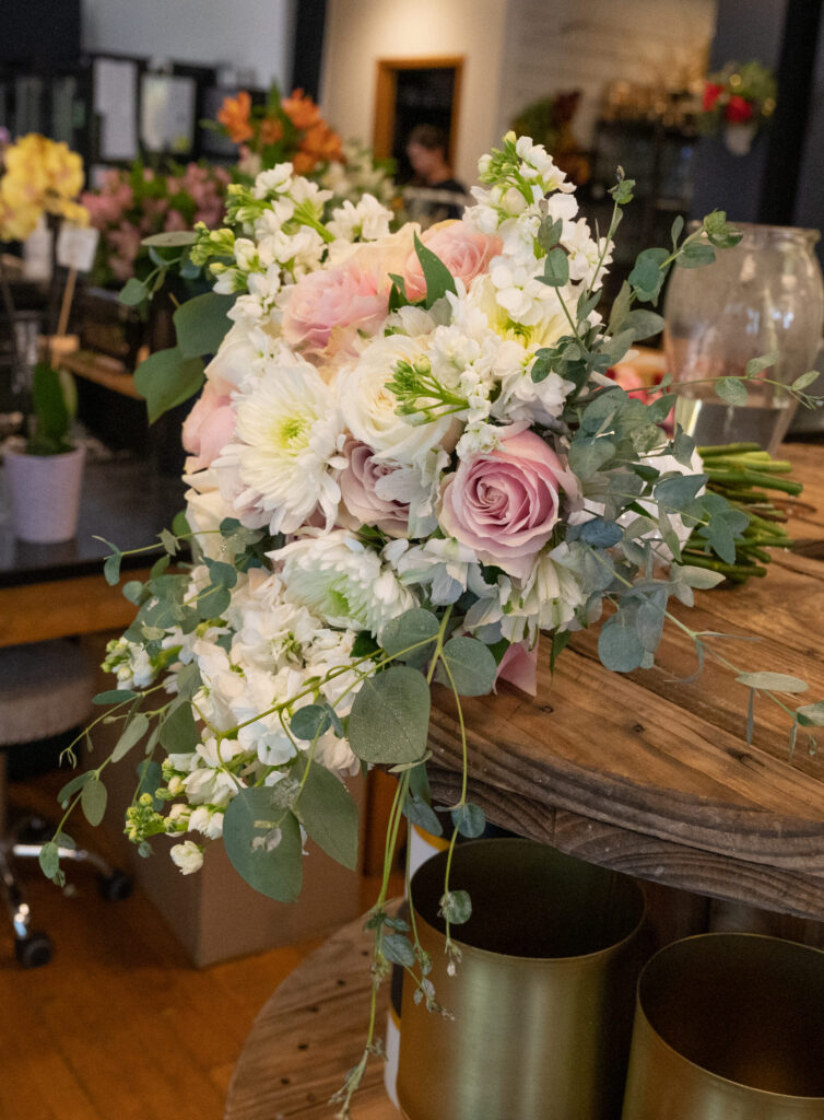 Bridal bouquet in flower shop featuring soft pink roses, white mums, and eucalyptus greenery