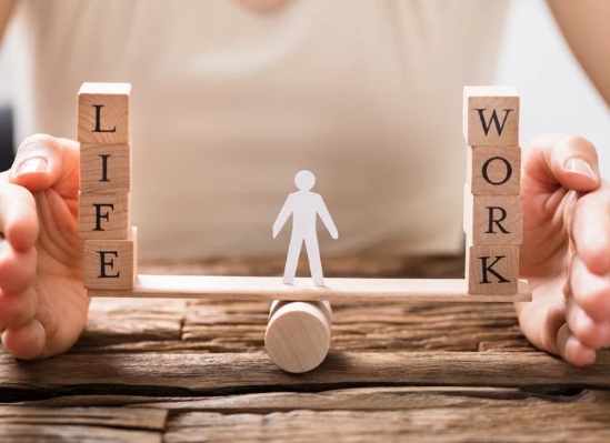 Wooden blocks spelling life and work balanced on a seesaw with a human figure in the middle, representing work-life balance and decision making.
