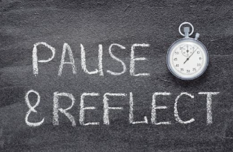 Chalkboard with the words pause and reflect written in white chalk next to a small silver stopwatch, representing taking time to reassess and plan.