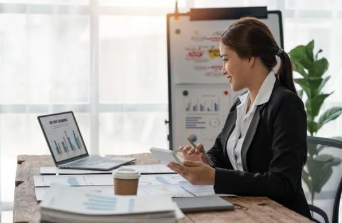Businesswoman in a white-collar outfit working at a desk with a laptop, tablet, and marketing charts in an office.