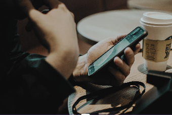 Person using a smartphone while holding a coffee cup in a cafe setting, focusing on social media marketing strategies.