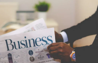 Man in a suit holding a newspaper with the headline "Business" in an office setting