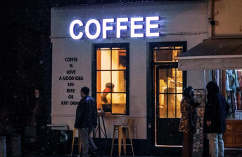 Exterior view of a lit-up coffee shop at night with people standing outside