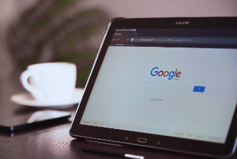 Tablet on table showing Google homepage, with a white cup and saucer beside it.