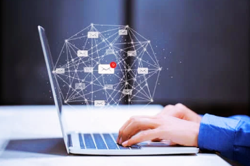 Hands typing on laptop with digital email network graphics overlay.