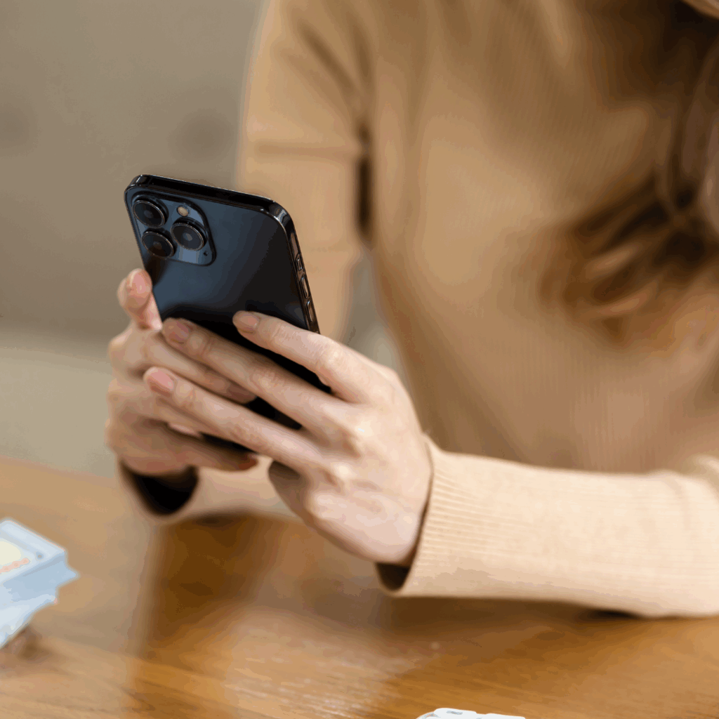 Woman wearing beige sweater holding a smartphone, sitting at a table.