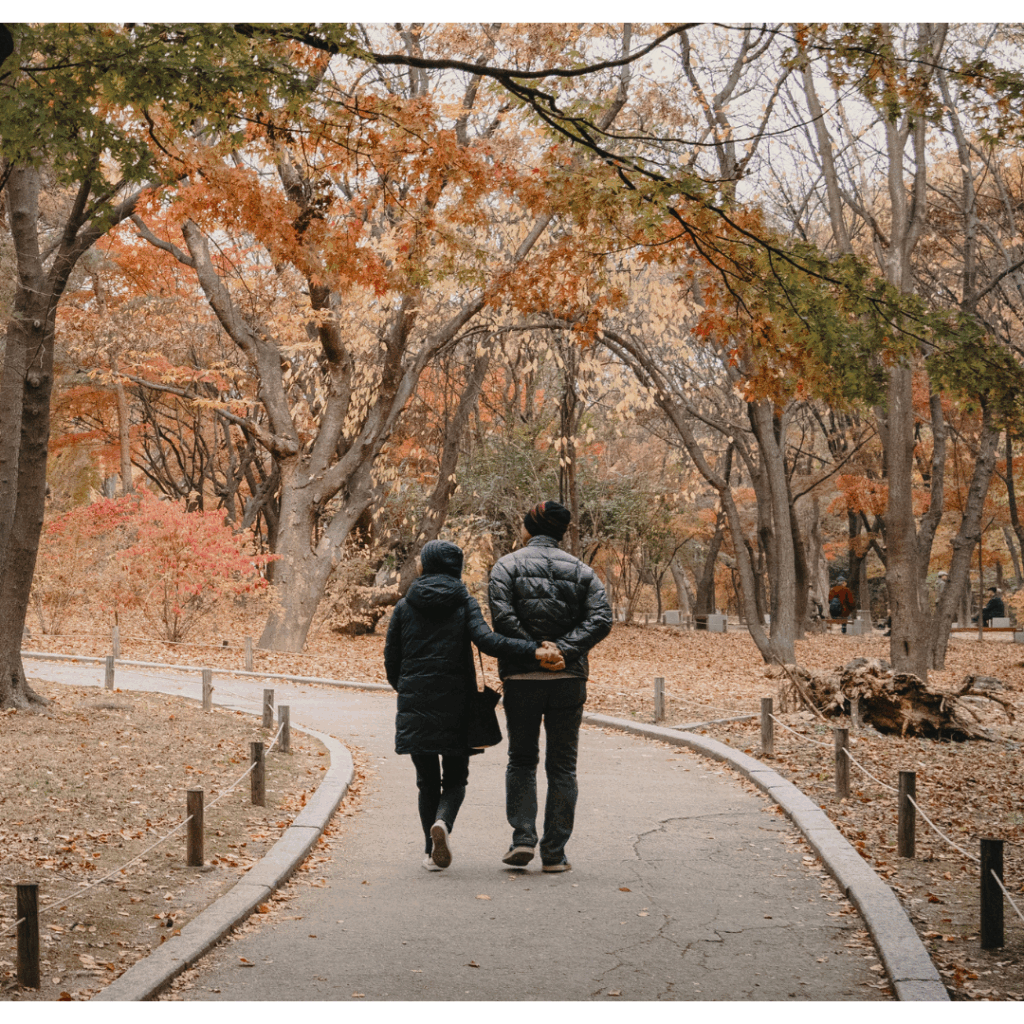 Couple walking together on a curved path in a park with autumn trees, representing support, reflection, and peaceful connection.