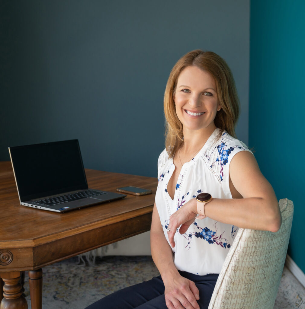Smiling female entrepreneur sitting confidently at her desk with a laptop and phone, representing calm productivity and approachable business leadership."