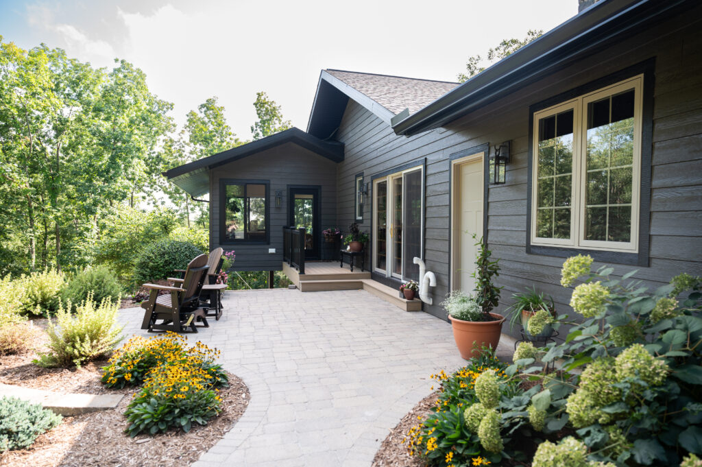 Custom home exterior view of remodel with blueish gray siding, paver path, and landscaping plants.